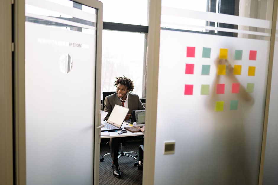 A team of professionals in a bright, modern office collaborates on a strategy mapped out with notes and lines on a glass wall, signifying advanced agency tactics.